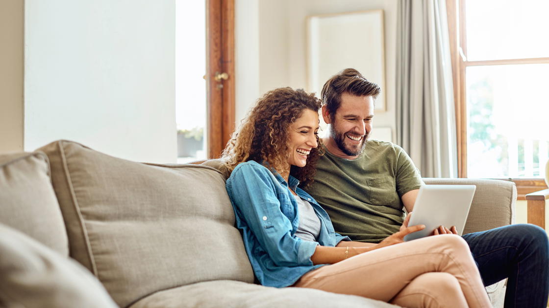Mann und Frau mit Laptop sitzen auf der Couch und lächeln
