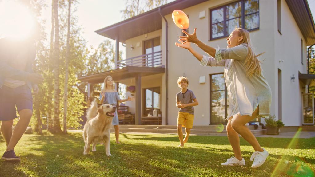 Familie spielt vor Haus Frisbee mit Hund